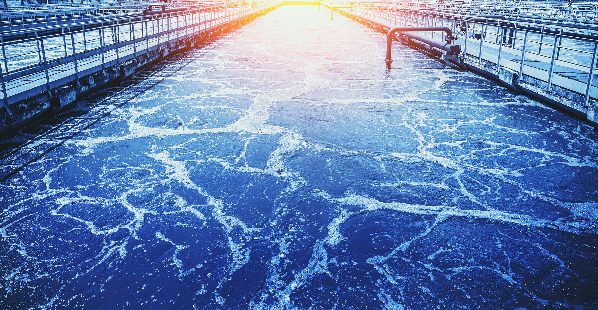 A long tank holds dark wastewater that has light bubbles across its surface
