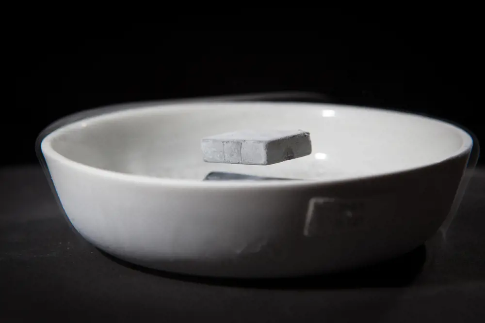 A solid chunk of grey material floating above a bowl with wispy, smoke-like liquid nitrogen around it