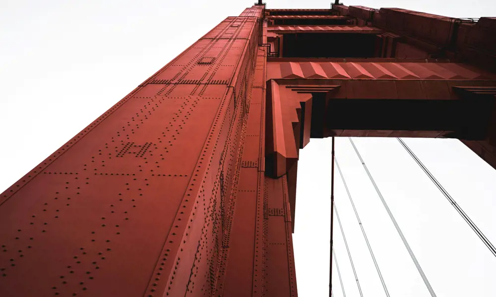 A worms-eye view of a red steel tower of the Golden Gate Bridge on an overcast day.