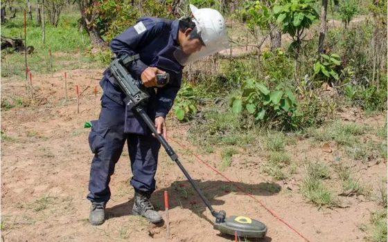 A male, wearing a face shield and protective equipment, with a dual-sensor detector in a field.