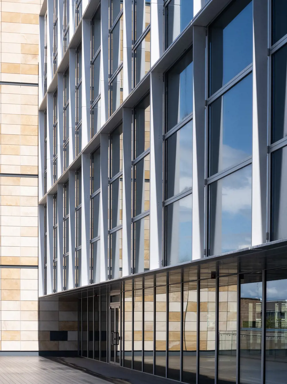 A side of the one Triton Square building in London covered in reflective windows next to a tiled wall.