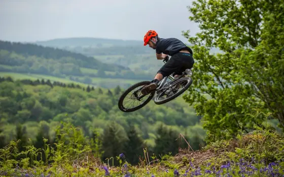 A person with a helmet riding a mountain bike in the air, with rolling green hills in the background. 