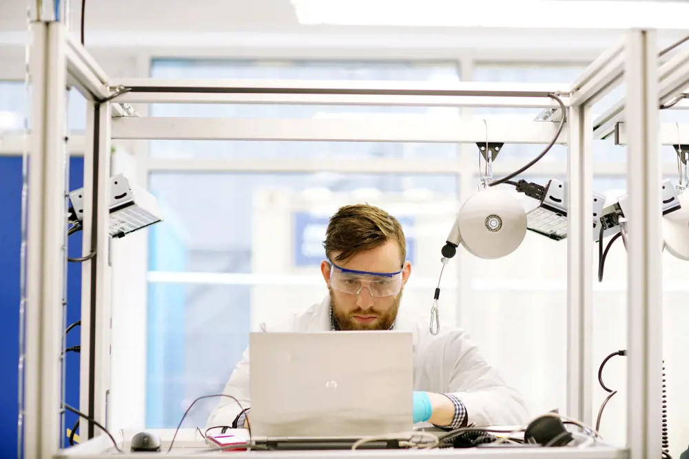 A scientist working on a laptop with expensive testing equipment around them.