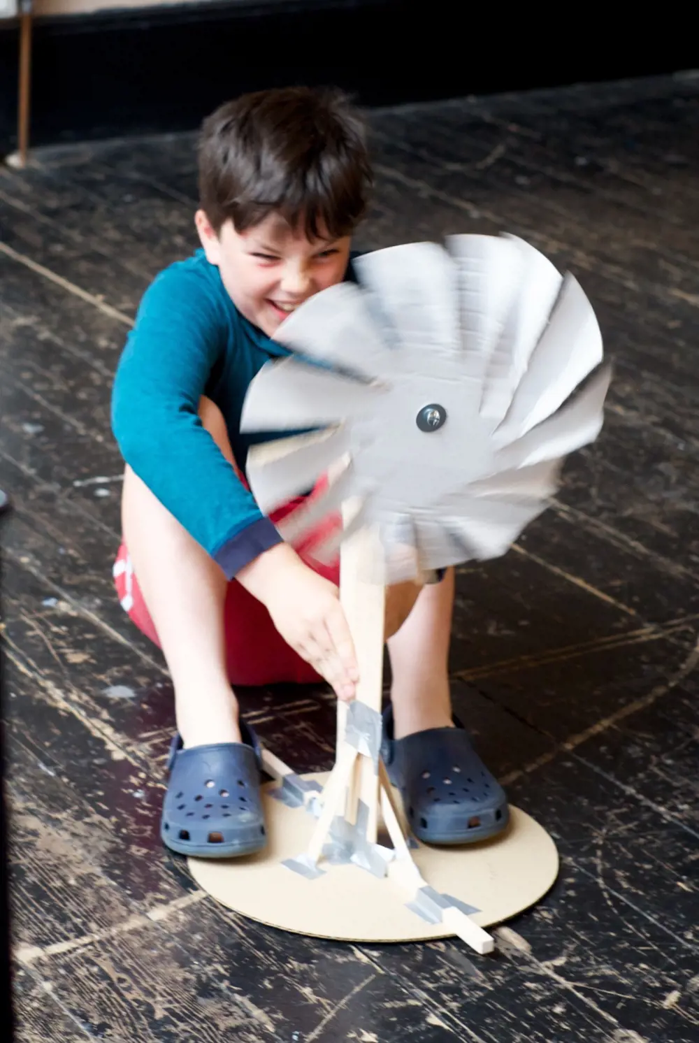 A child sitting on the floor, holding a spinning wind turbine. 