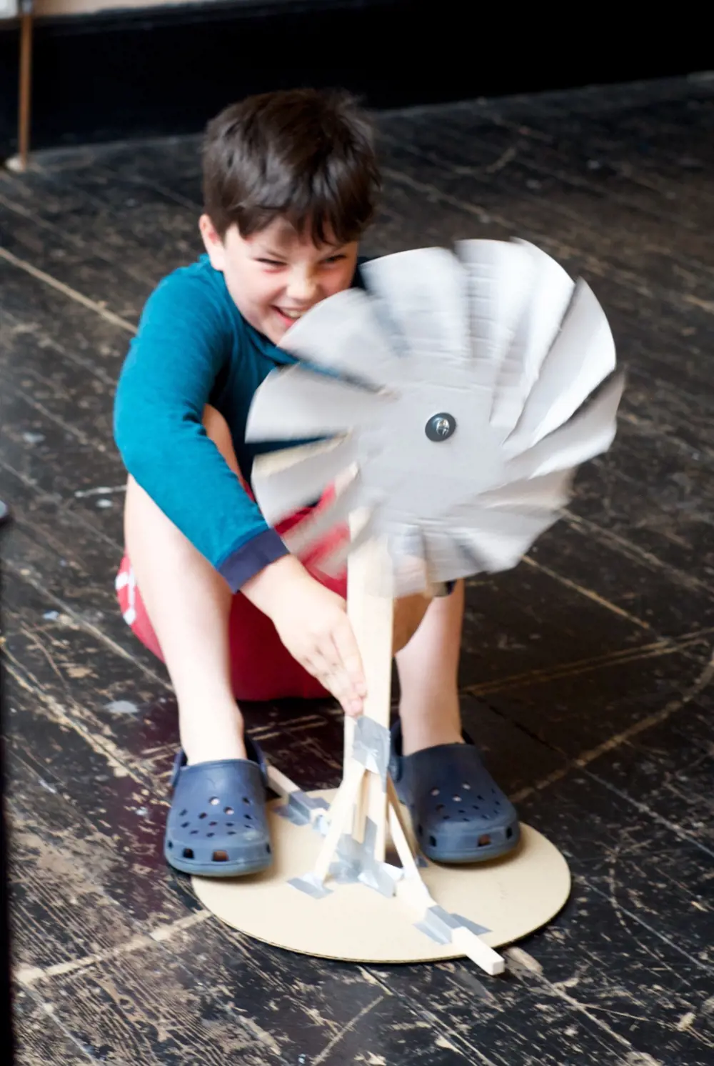 A child sitting on the floor, holding a spinning wind turbine.