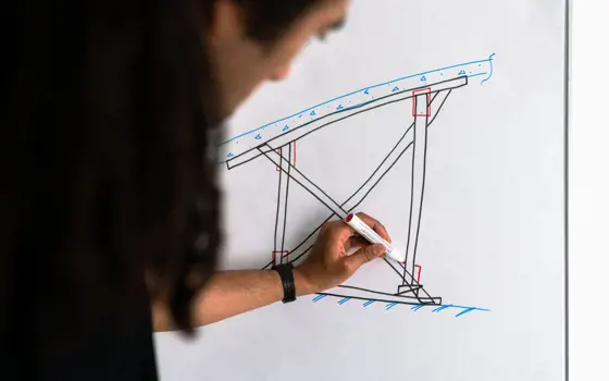 Male structural engineer draws on whiteboard.