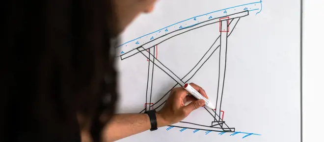 Male structural engineer draws on whiteboard.