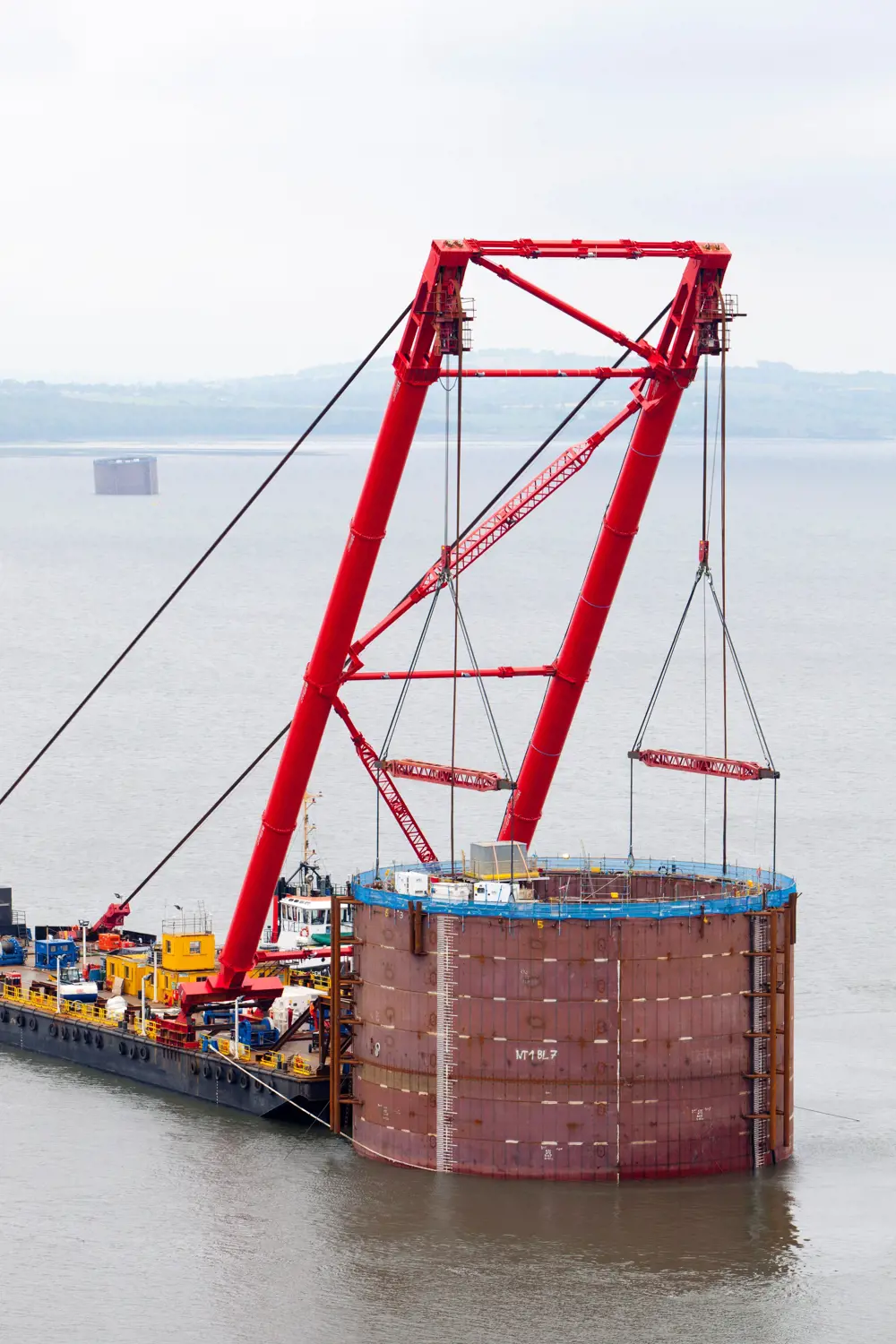 A cylindrical caisson attached to a crane in water.