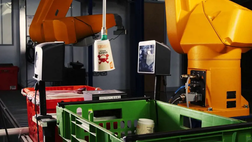 A plastic crate sitting underneath a suction cup attached to a robotic arm that is used to grasp onto objects.