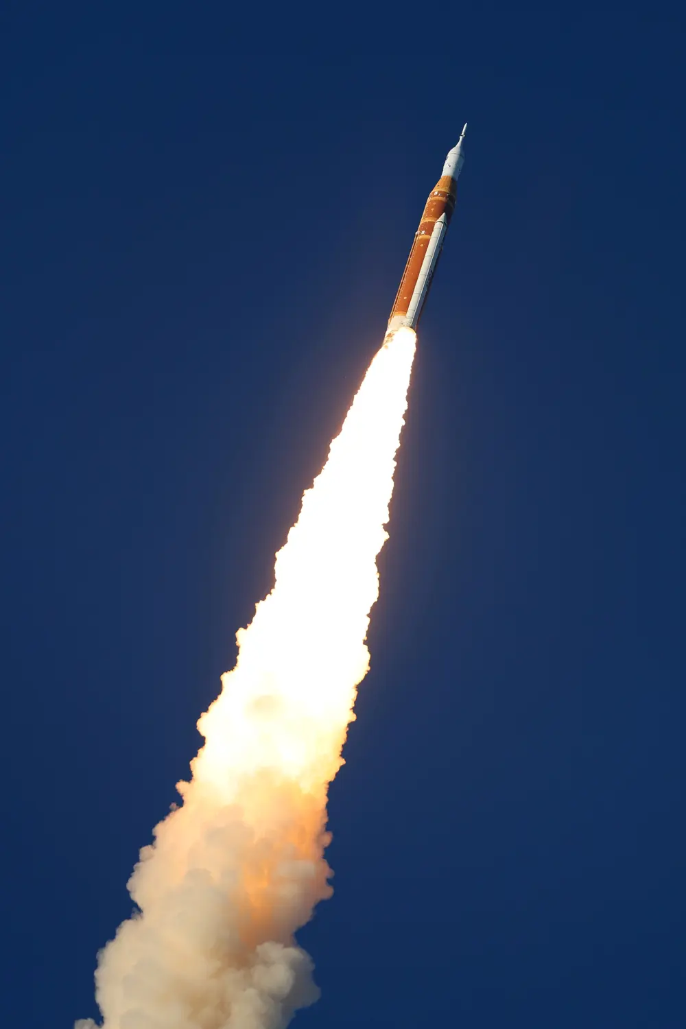Heavy-lift rocket launching with bright exhaust plume, climbing into a clear blue sky.