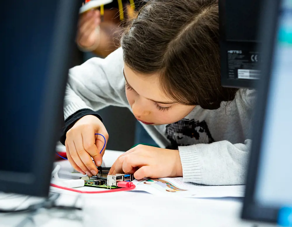A young girl at school works intently using a Raspberry Pi computer