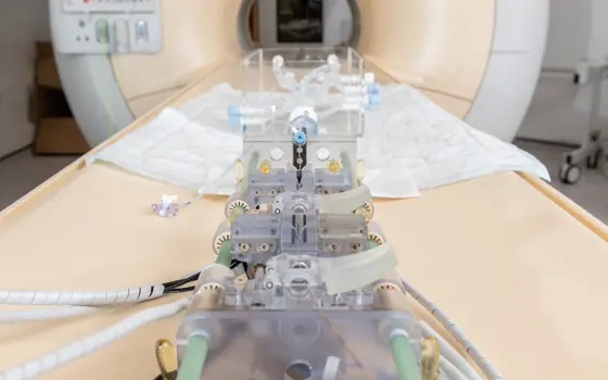 A robot on a CT scanner patient table, which has wires and tubing to adjust guidewires and catheters.