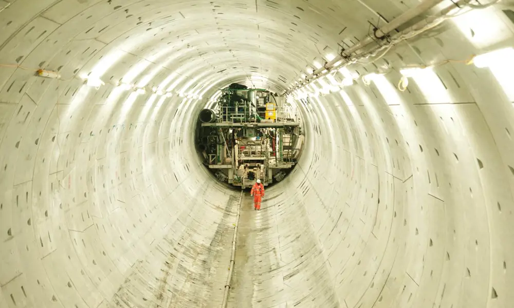 A person in a high visibility suit standing in a brightly lit large underground tunnel. 