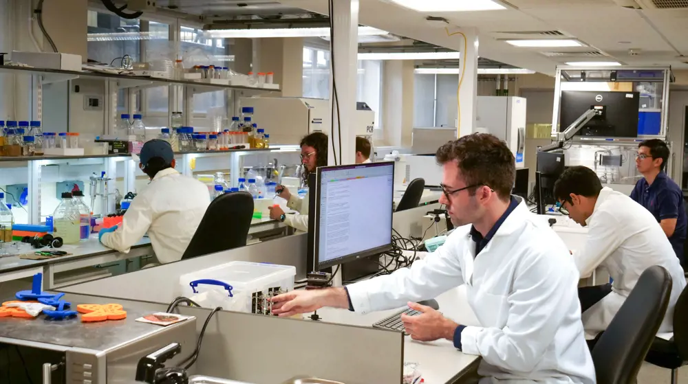 Dr Harrison Steele working inside a lab, at a lab bench, with other researchers working near him.