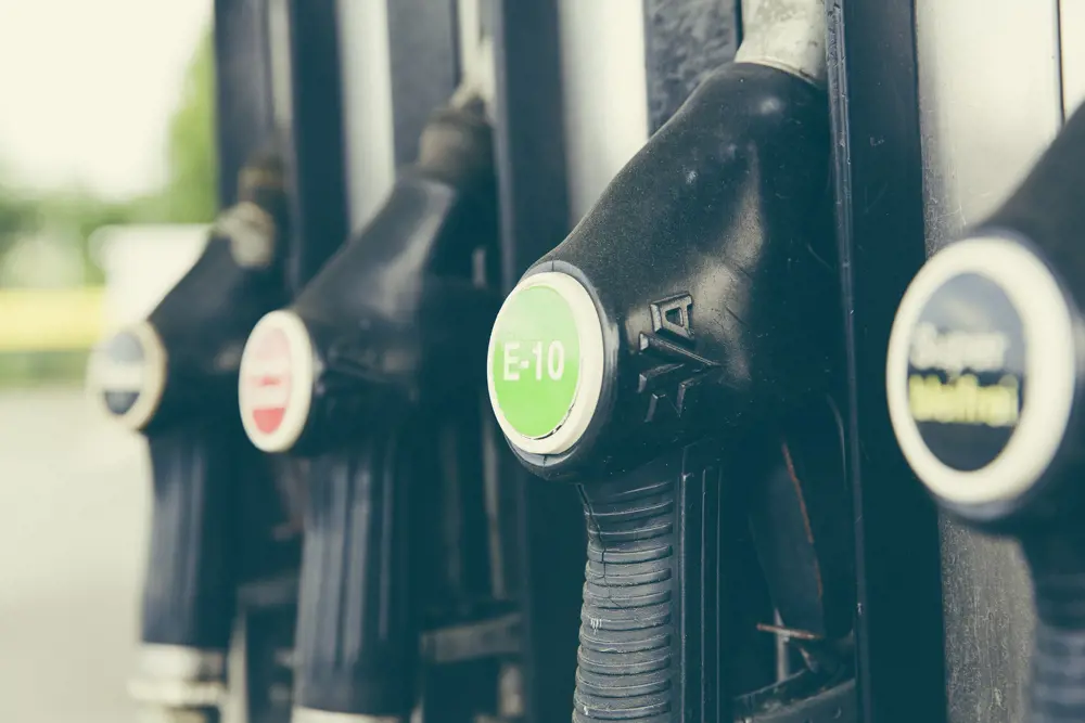 Four fuel dispensers at a petrol station, with different brands of fuel. The fuel dispenser with the E10 biofuel labelled on the handle is in focus. 