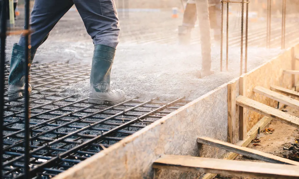 A construction worker is pouring a concrete onto a reinforced metal grid.