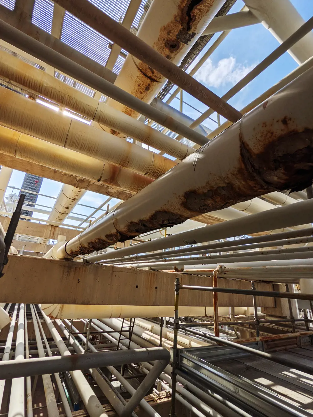 Pipework at a refinery where deep brown rust has become visible at the base of each of the pipes.