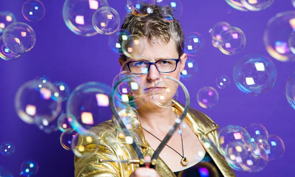 A photo of Lucy Rogers holding an engineered metal bubble maker, surrounded by bubbles